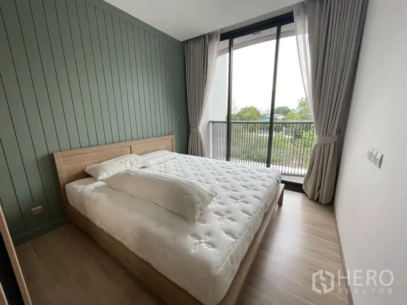 公寓 出租在Watthana, Bangkok - 主卧配大床与装饰墙，连通阳台可观树景。