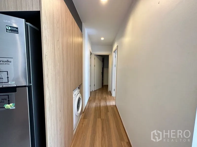 Condominium for rent in Watthana, Bangkok - Hallway with built-in cabinetry, a recessed washing machine, and doors to bedrooms and bathrooms.