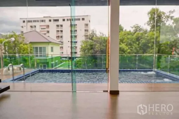 独立式住宅 出售在Lat Phrao, Bangkok - 透过玻璃墙看到私家泳池，背景为公寓楼景色。