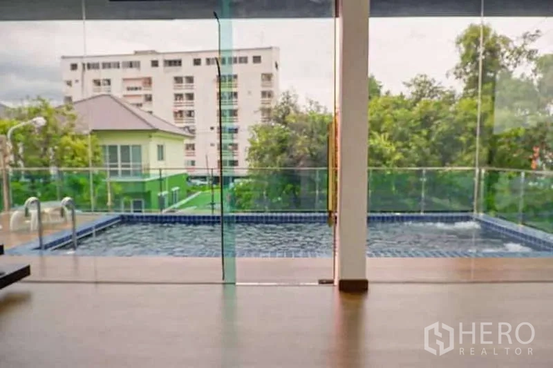 独立式住宅 出售在Lat Phrao, Bangkok - 透过玻璃墙看到私家泳池，背景为公寓楼景色。