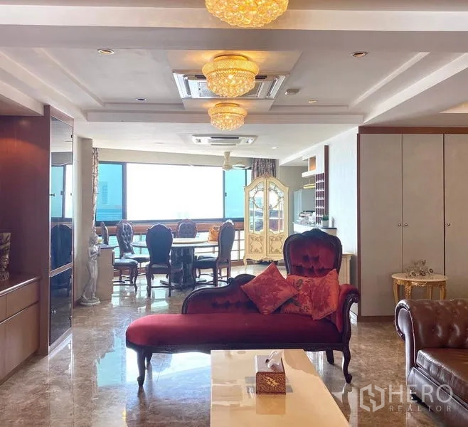Condominium for rent in Khlong Toei, Bangkok - Living room leading to dining area with a red chaise lounge and wide windows.