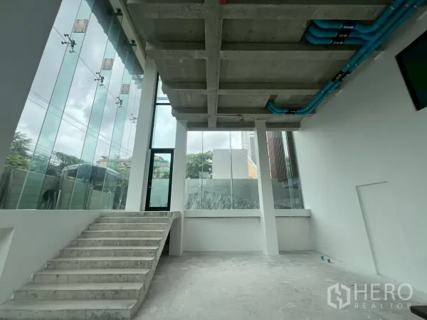 Retail Space for rent - Double-height ground floor interior with concrete stairs and floor-to-ceiling windows.
