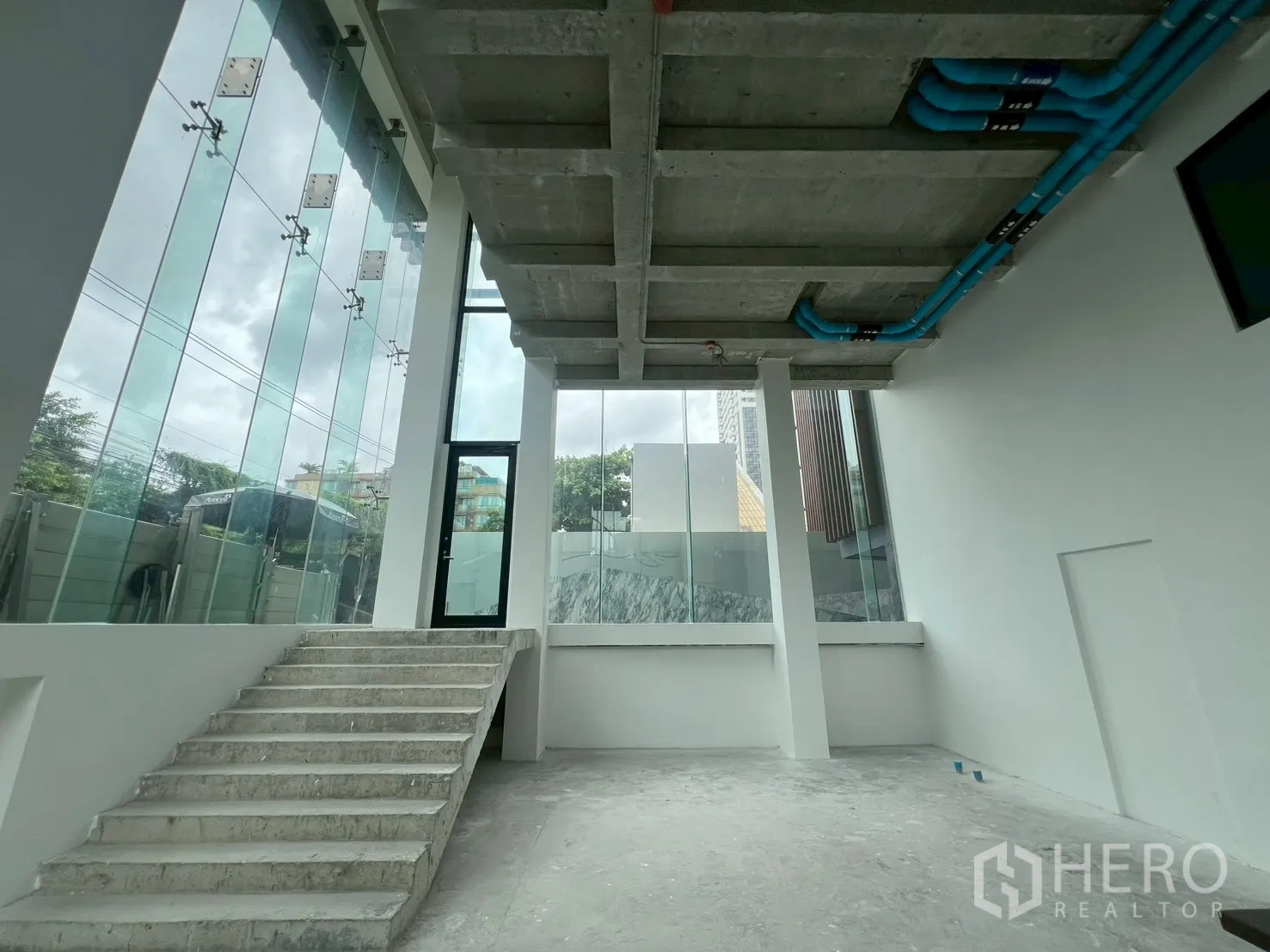 Retail Space for rent - Double-height ground floor interior with concrete stairs and floor-to-ceiling windows.