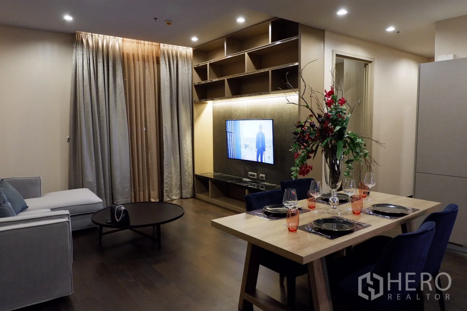 คอนโด ให้เช่าในWatthana, Bangkok - พื้นที่นั่งเล่นและทานอาหารแบบเปิดโล่ง ผนังทีวีบิวท์อิน ชั้นวาง พื้นไม้ และผ้าม่านเต็มความสูง