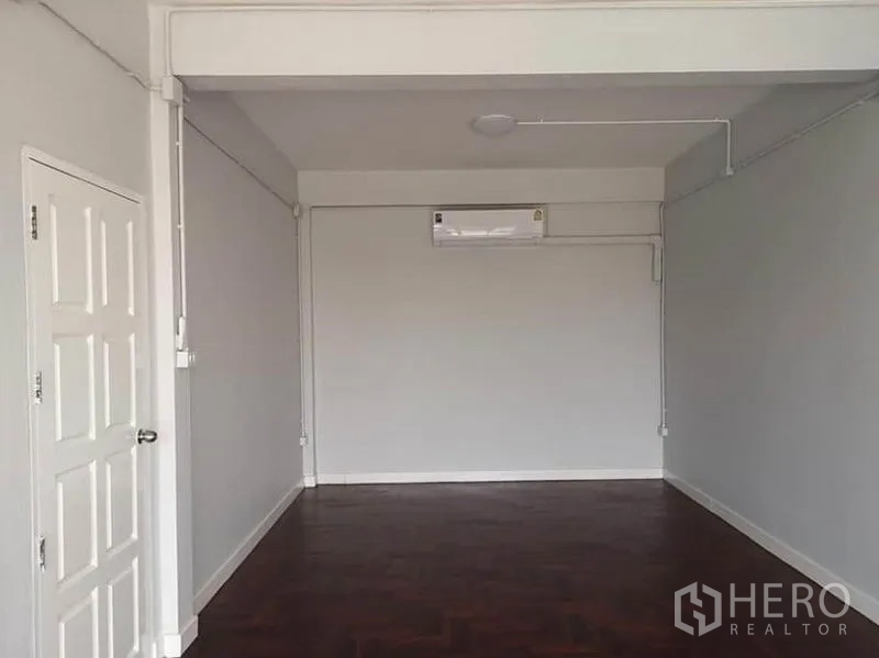 Townhouse for rent or sale in Din Daeng, Bangkok - Spacious room with air conditioner, white walls, and parquet flooring suitable for a bedroom or office.