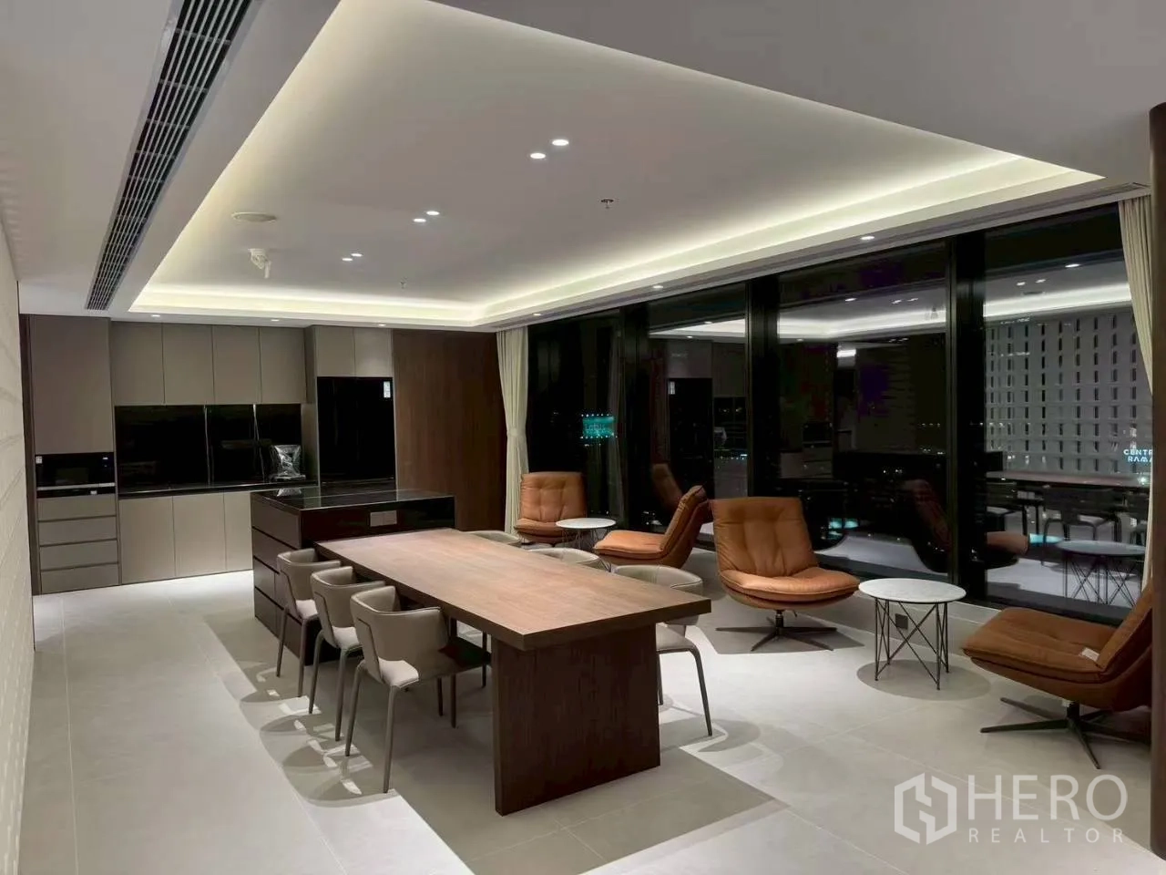 Office Space for rent in Din Daeng, Bangkok - Pantry and breakout area with long table, lounge chairs, and floor-to-ceiling windows at night.