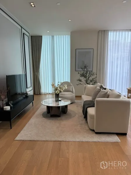 Condominium for rent in Pathum Wan, Bangkok - Bright living room with cream sofa, marble coffee table, TV console, and sheer curtains.