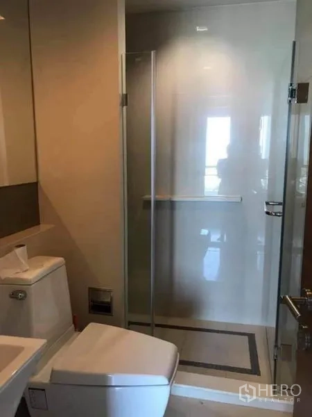 Condominium for rent or sale in Phaya Thai, Bangkok - Light bathroom with glass shower cubicle, toilet and vanity.