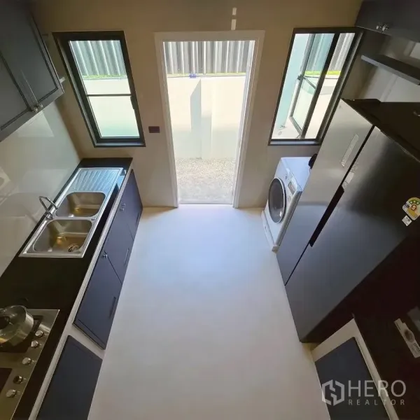 Detached House for rent in Bang Phli, Samut Prakan - Galley kitchen with dual sink, cooktop, fridge, washer, and rear door.