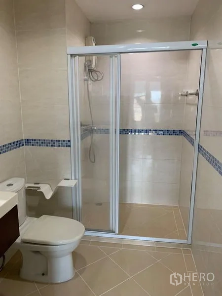 Condominium for rent in Bang Rak, Bangkok - Second bathroom with glass-enclosed shower, toilet and beige floor tiles.