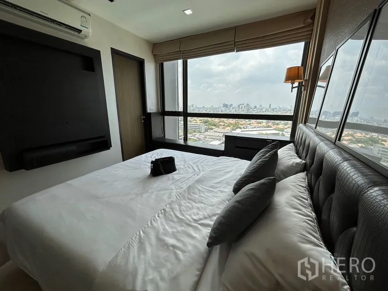 Condominium for rent or sale in Khlong Toei, Bangkok - Bedroom corner with full-height windows showcasing panoramic Bangkok skyline views.