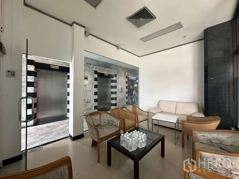 Retail Space for rent - Cozy waiting area with armchairs and coffee table next to stainless-steel elevators in a commercial lobby.