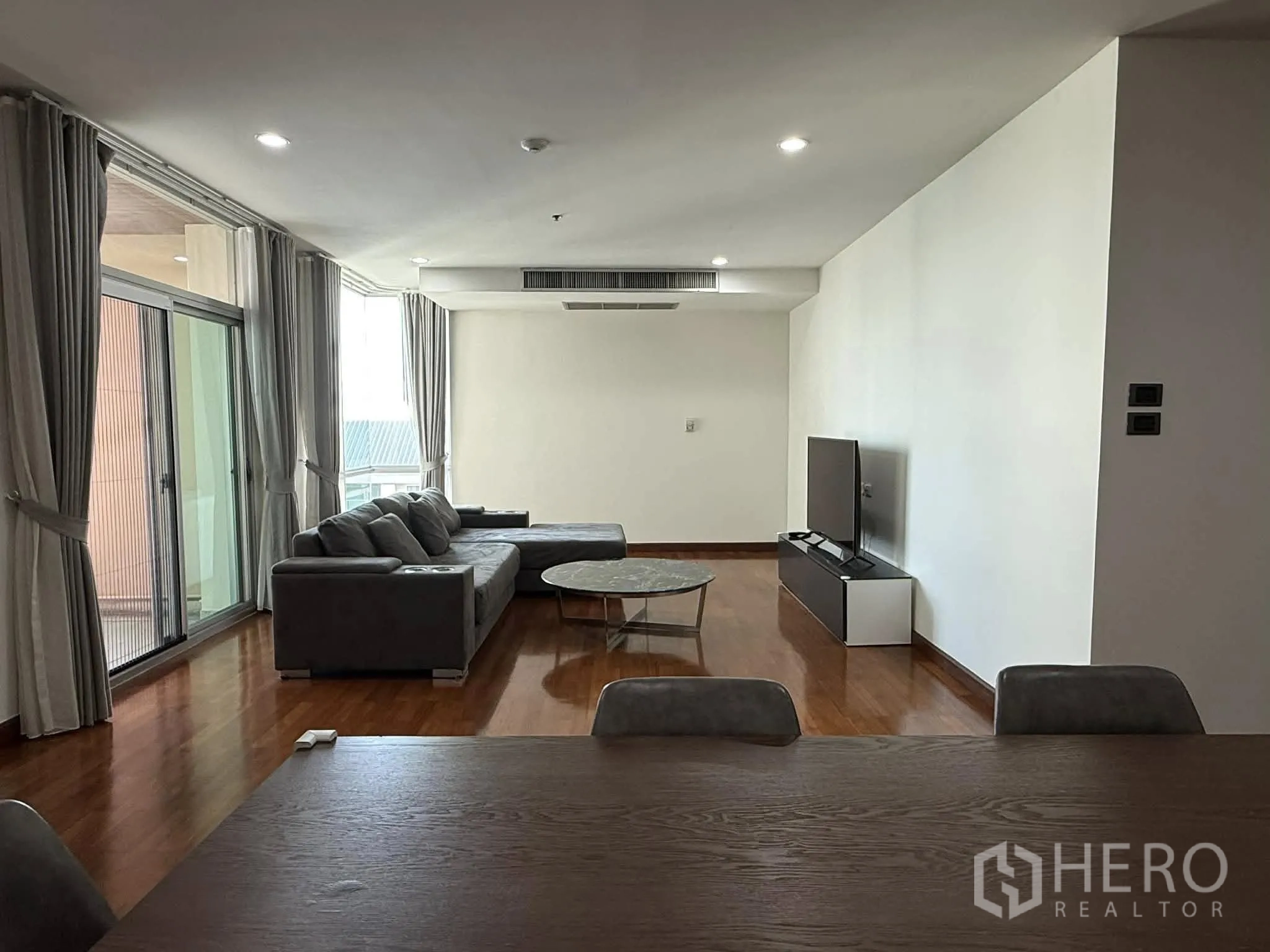 Condominium for rent in Pathum Wan, Bangkok - Lounge with sliding glass doors to the balcony, full-length curtains, and ceiling lights.