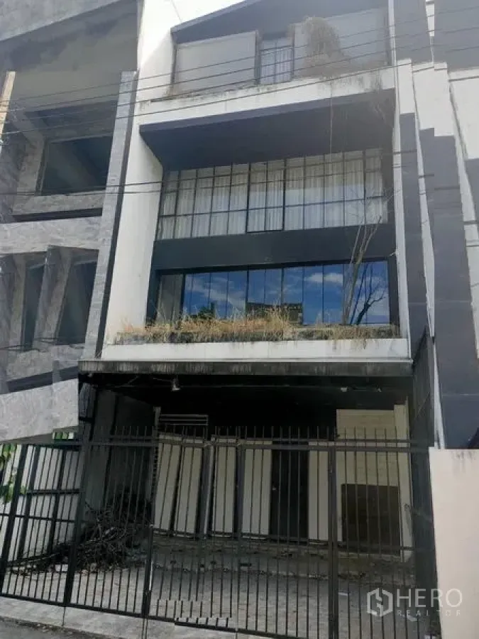 带办公室的家 出租在Watthana, Bangkok - 多层家办楼外立面，黑白配色，带围栏车位与阳台绿植。