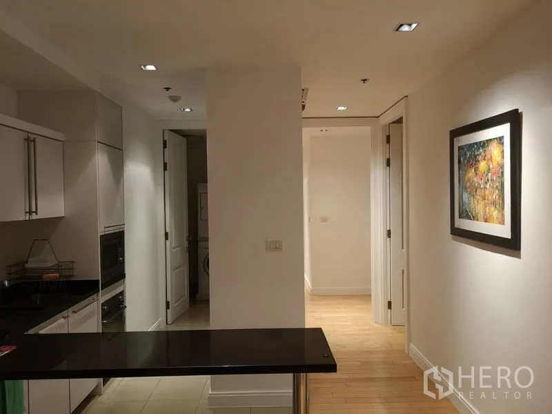 Condominium for rent in Pathum Wan, Bangkok - Hallway view from kitchen toward bedrooms with recessed lighting and framed artwork.