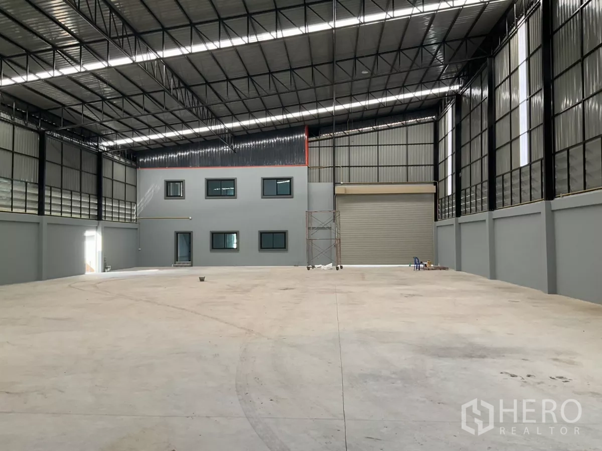 Factory for sale in Samut Sakhon - Spacious warehouse interior with high clear-span steel truss roof, roller shutter door and smooth concrete floor.