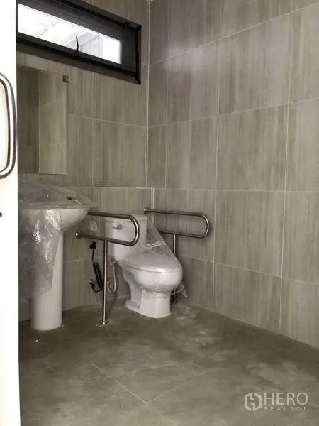 Factory for rent or sale in Samut Prakan - Tiled restroom equipped with accessibility grab bars and a window.