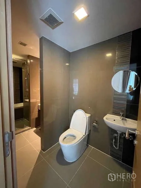 Condominium for sale in Watthana, Bangkok - Second bathroom with toilet and compact sink leading to the shower area.