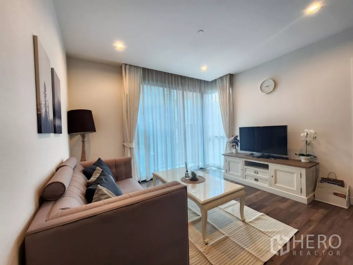 Condominium for rent in Phra Khanong, Bangkok - Living room with sofa, coffee table, TV console, and full-height sheer curtains.