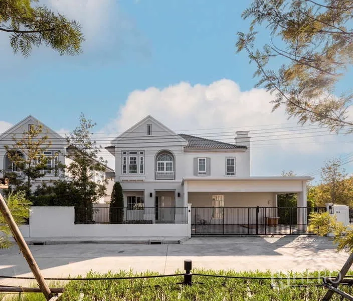 Detached House for rent or sale in Bang Phli, Samut Prakan - Front view of a two-storey white detached house with gated carport and landscaped yard under a blue sky in Bang Phli.
