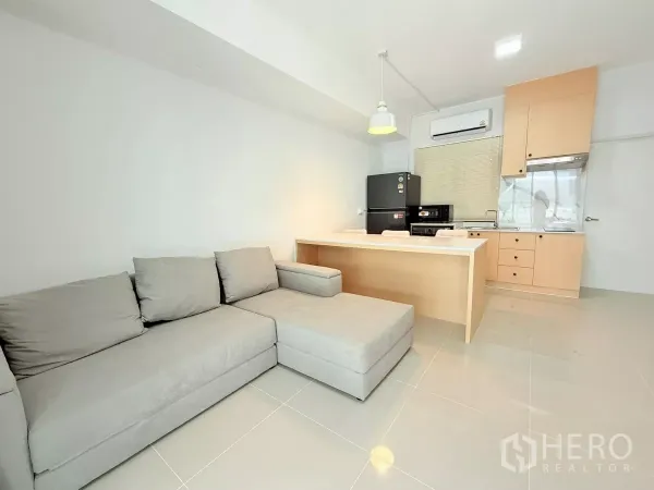 Townhouse for rent in Bang Phli, Samut Prakan - Spacious lounge with L-shaped sofa facing a peninsula kitchen and large tiled flooring.