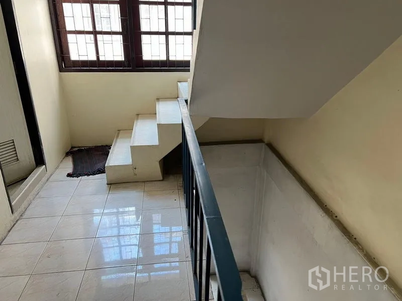 Shophouse for sale in Phra Khanong, Bangkok - Bright stair landing with tiled floor, metal railing and large grilled windows.