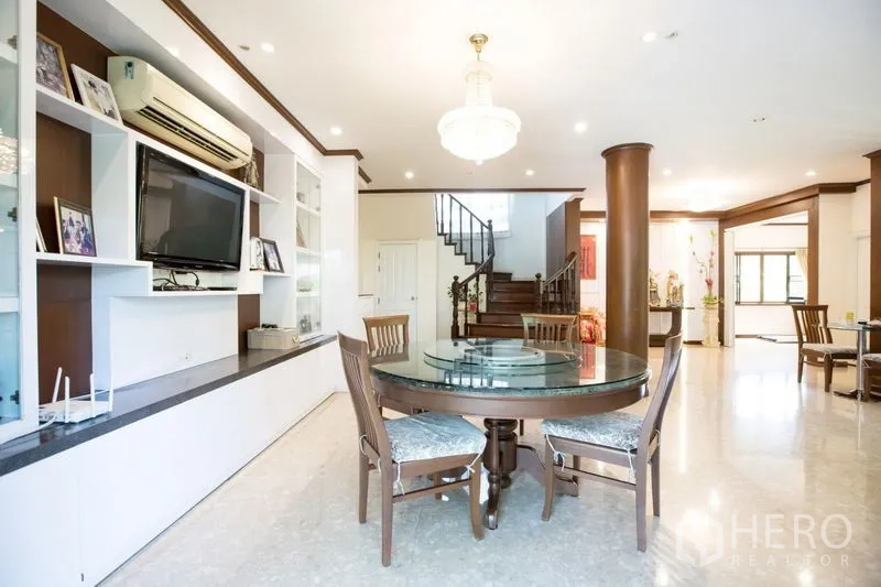 Detached House for sale in Lat Krabang, Bangkok - Dining area with round table, chandelier, built-in shelving and staircase backdrop.