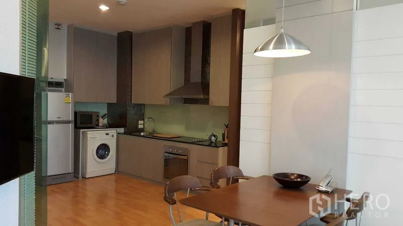 Condominium for rent in Khlong Toei, Bangkok - Open-plan kitchen and dining area with pendant light, washing machine and full-size fridge.