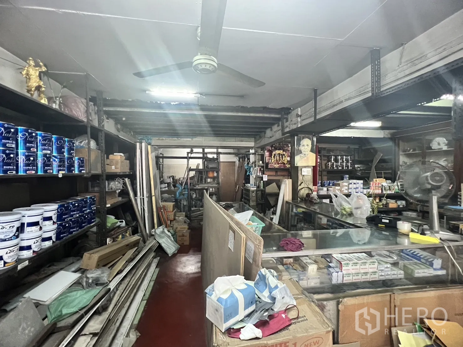 Retail Space for rent in Watthana, Bangkok - Main shop aisle with long counter, ceiling fan and rows of paint on steel shelving.