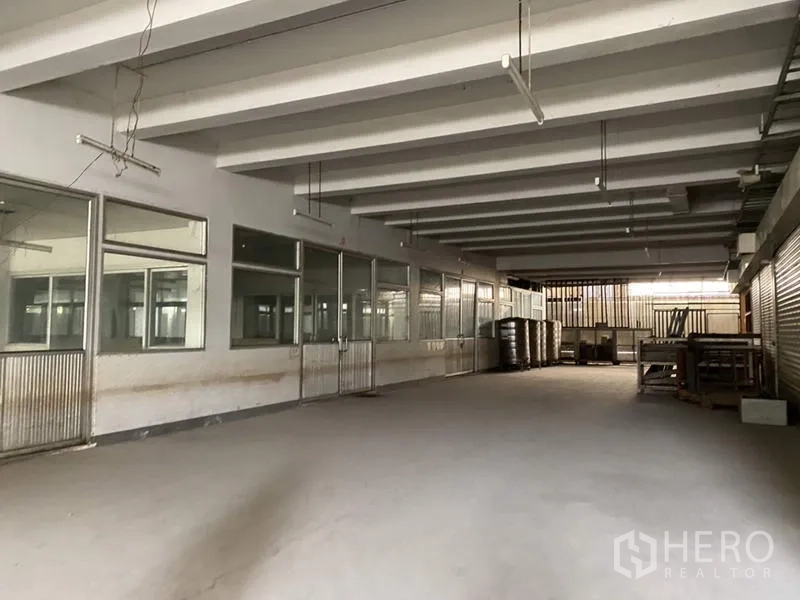 Factory for sale in Khlong Luang, Pathum Thani - Enclosed service area with interior windows and roller shutters at the rear.