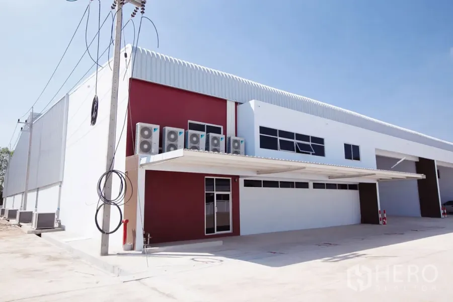 Factory for rent in Si Racha, Chon Buri - Modern factory exterior with canopy entrance, AC condenser units, and paved yard.
