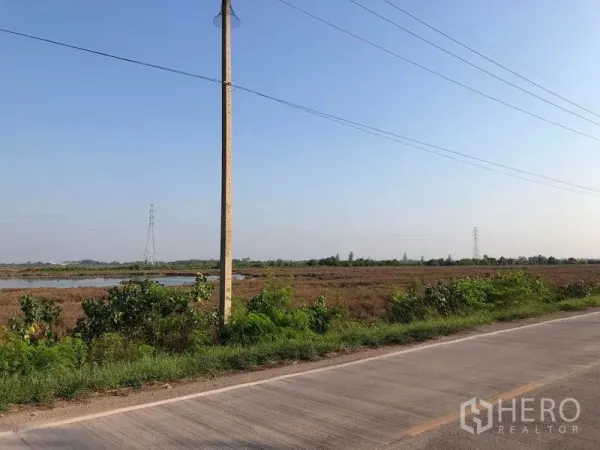 Land for sale in Mueang Samut Sakhon, Samut Sakhon - Main-road frontage with utility pole and paved access facing a large open land parcel.