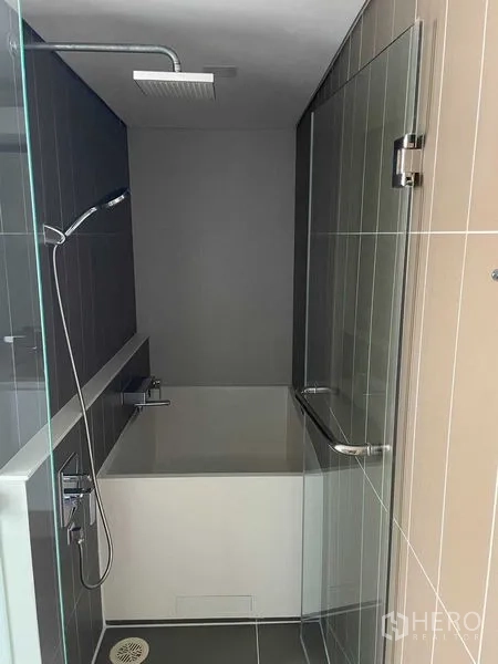 Condominium for rent in Khlong Toei, Bangkok - Shower room with bathtub, rain shower and glass door in neutral tiles.
