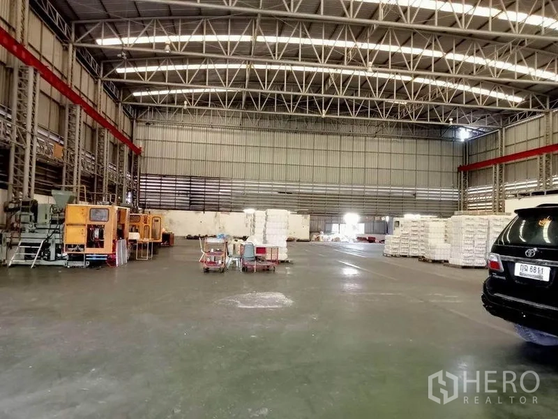工厂 出租在Bang Phli, Samut Prakan - 宽敞厂房，高钢结构屋顶，混凝土地面，部分设备与托盘。