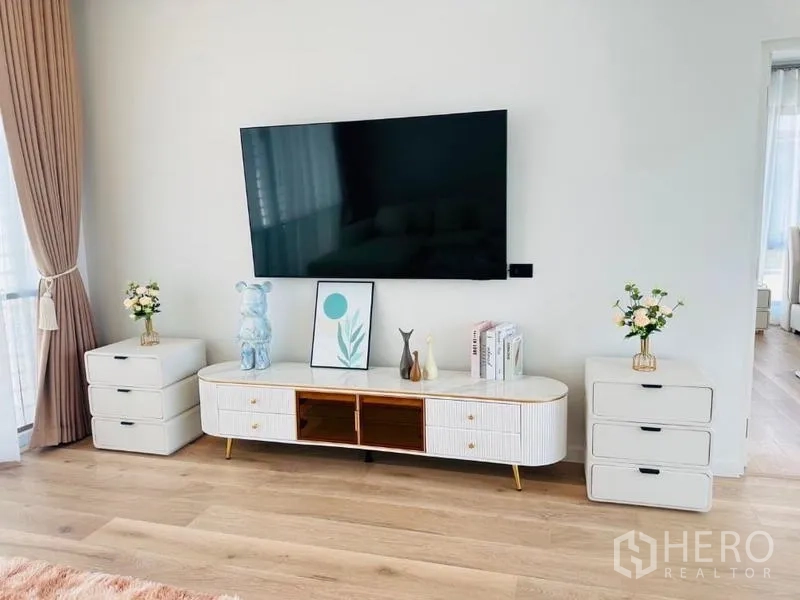 Detached House for rent or sale in Bang Kapi, Bangkok - Living room media wall with mounted TV, white console cabinets and light wood flooring.