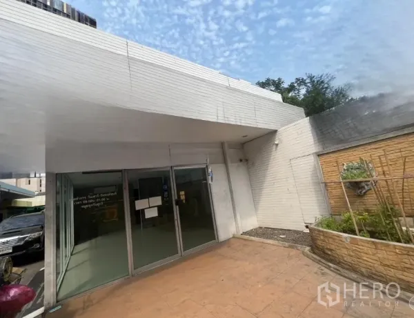 零售空间 出租在Khlong Toei, Bangkok - 店面斜角视图，前方有铺装步道与花坛。