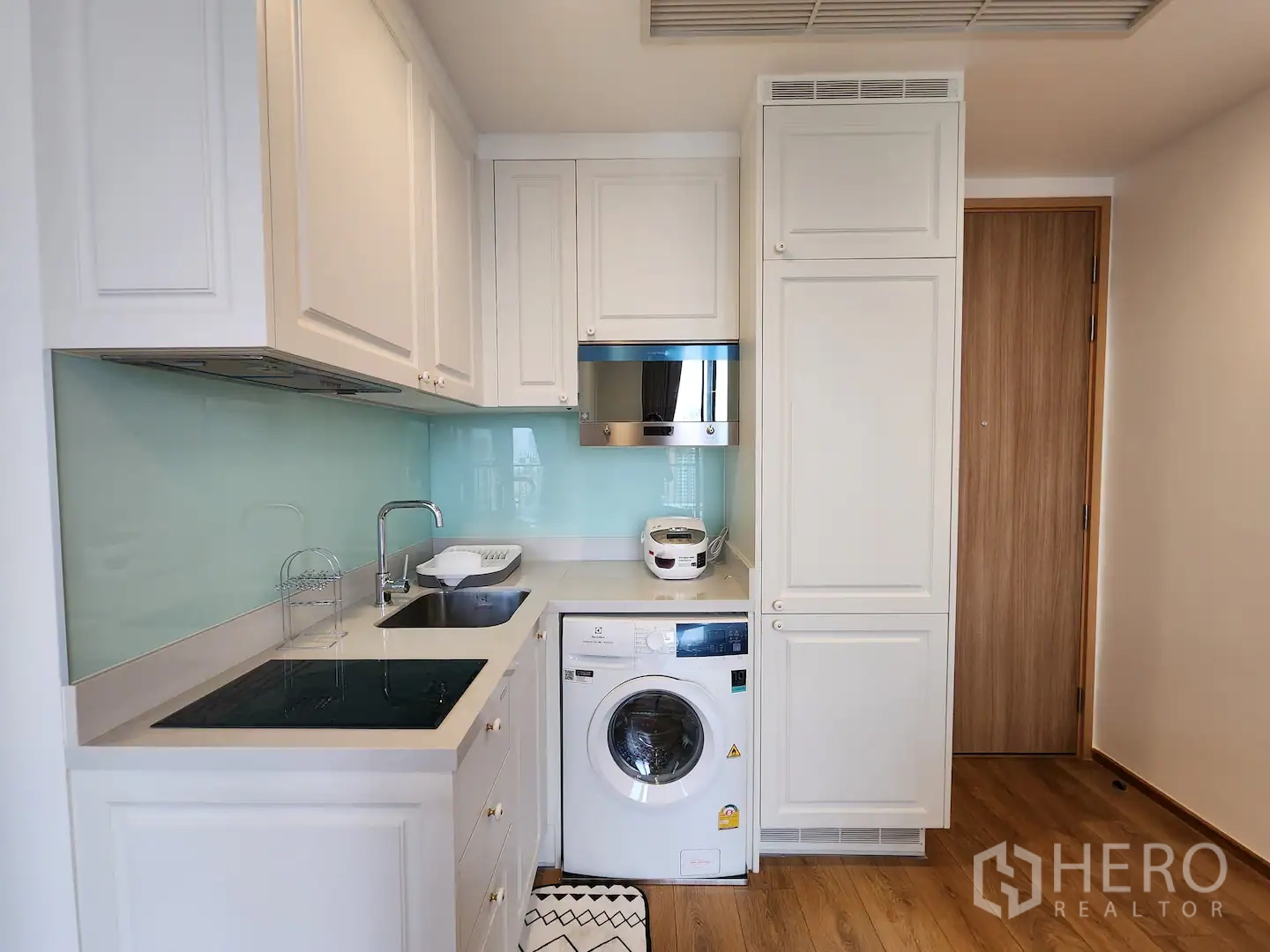 Condominium for rent in Watthana, Bangkok - Close-up of the fitted kitchen showing built-in cabinets, cooktop, microwave and washing machine.
