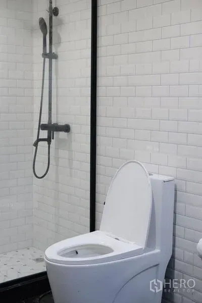Condominium for rent in Bang Rak, Bangkok - Modern bathroom with white subway tiles, glass shower and toilet.
