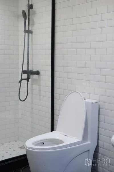 Condominium for rent in Bang Rak, Bangkok - Modern bathroom with white subway tiles, glass shower and toilet.