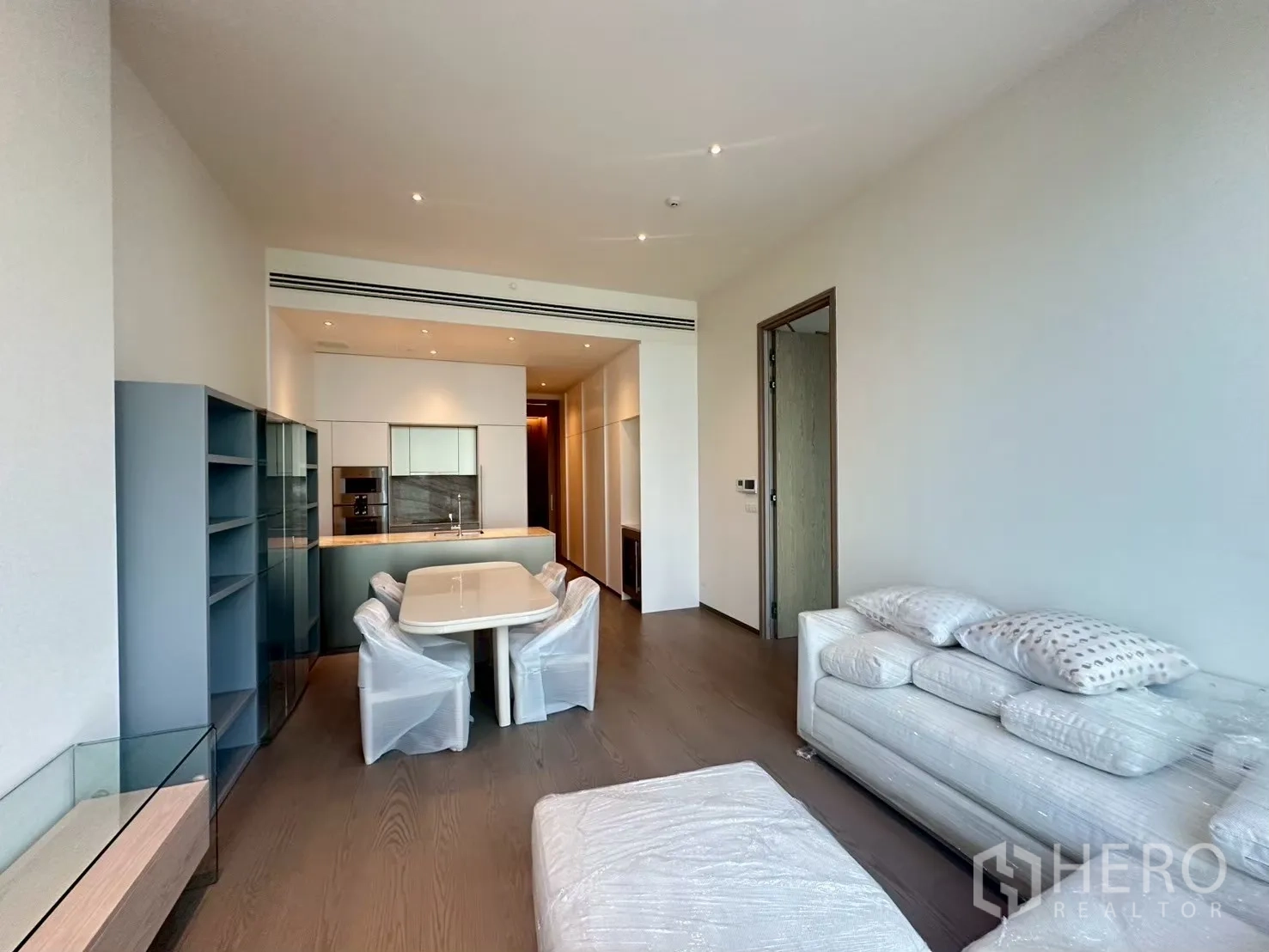 คอนโด for rent in Pathum Wan, Bangkok - พื้นที่นั่งเล่นและทานอาหารแบบโอเพ่นแพลน พร้อมครัวบิลท์อิน ชั้นวางบิลท์อิน พื้นไม้ โต๊ะทานอาหาร และโซฟา.