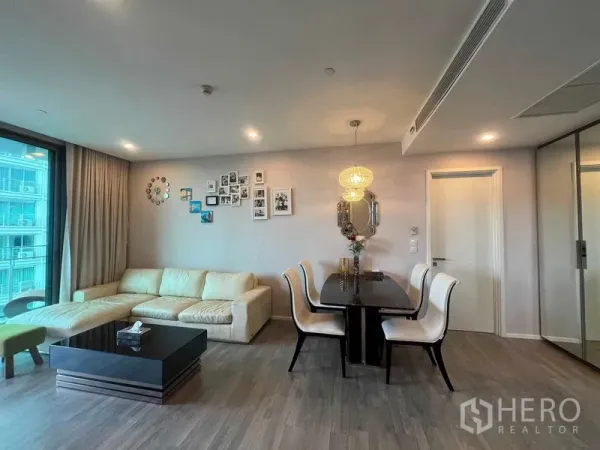 Condominium for rent in Khlong Toei, Bangkok - Open-plan living and dining area with chandelier, cream sofa and wood floors.
