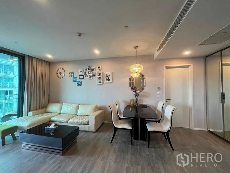 Condominium for rent in Khlong Toei, Bangkok - Open-plan living and dining area with chandelier, cream sofa and wood floors.