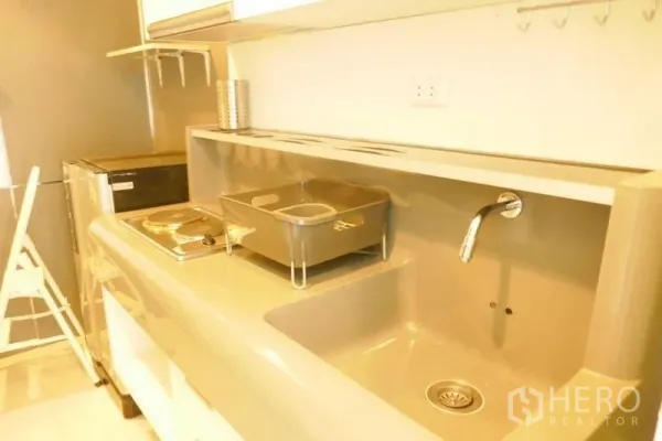 Condominium for rent or sale in Khlong San, Bangkok - Compact kitchenette with sink, electric cooktop, fridge and glossy backsplash.