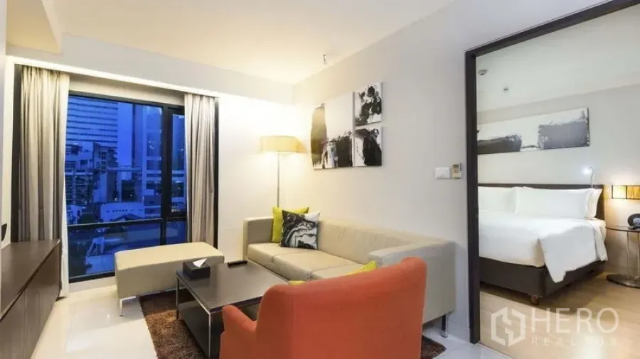อพาร์ทเมนท์ ให้เช่าในWatthana, Bangkok - ห้องนั่งเล่นสว่างพร้อมหน้าต่างวิวเมือง โซฟาและเก้าอี้สีส้ม ติดกับห้องนอน.