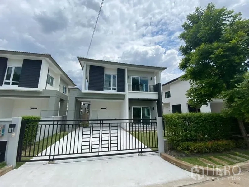 Detached House for rent in Khlong Luang, Pathum Thani - Front elevation of the home with wide driveway, lawn and tree-lined street.