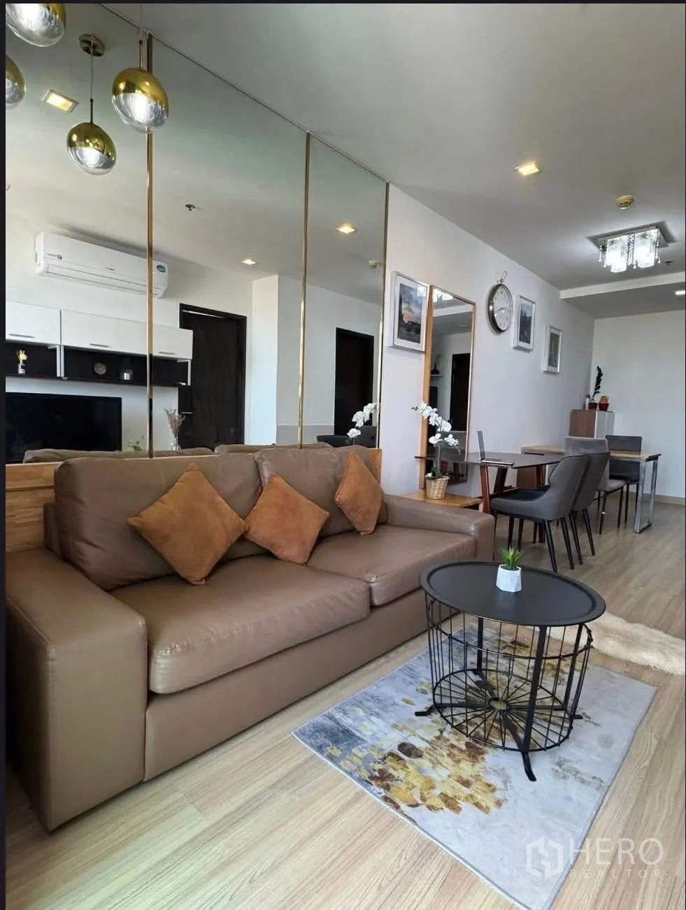 คอนโด for rent in Watthana, Bangkok - มุมนั่งเล่นพร้อมโซฟาหนังสีน้ำตาล ผนังกระจกเงา และโคมไฟแขวนข้างโต๊ะอาหาร