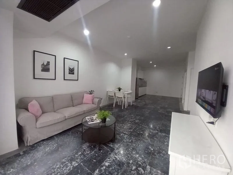 公寓 for rent in Watthana, Bangkok - 开放式客厅，沙发、餐桌、壁挂电视与深色石材地面。