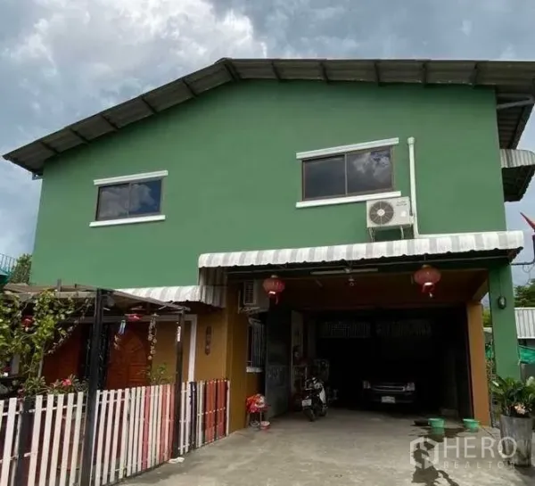 货栈 出租或出售在Pak Kret, Nonthaburi - 绿色两层建筑正面，条纹雨棚、车道停车位及墙挂式空调外机。