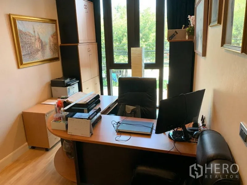 Townhouse for rent or sale in Chatuchak, Bangkok - Home office with desk, storage cabinets and tall windows overlooking greenery.