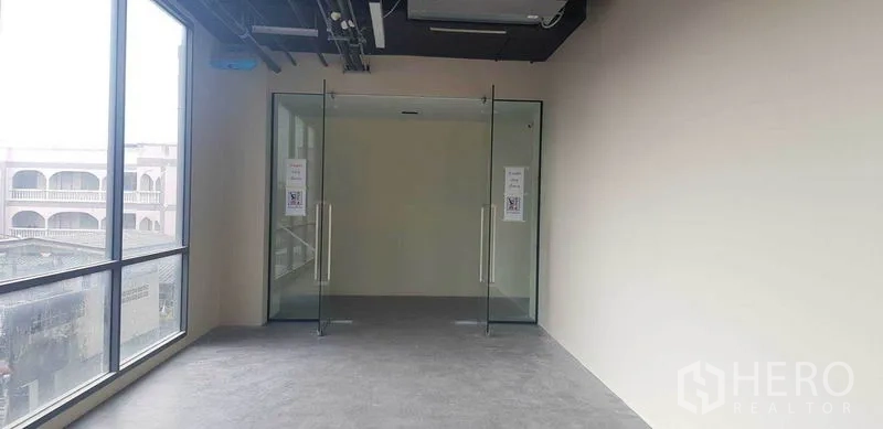 Office Space for rent in Suan Luang, Bangkok - Empty office interior with large window wall, double glass entry doors, and exposed ceiling.